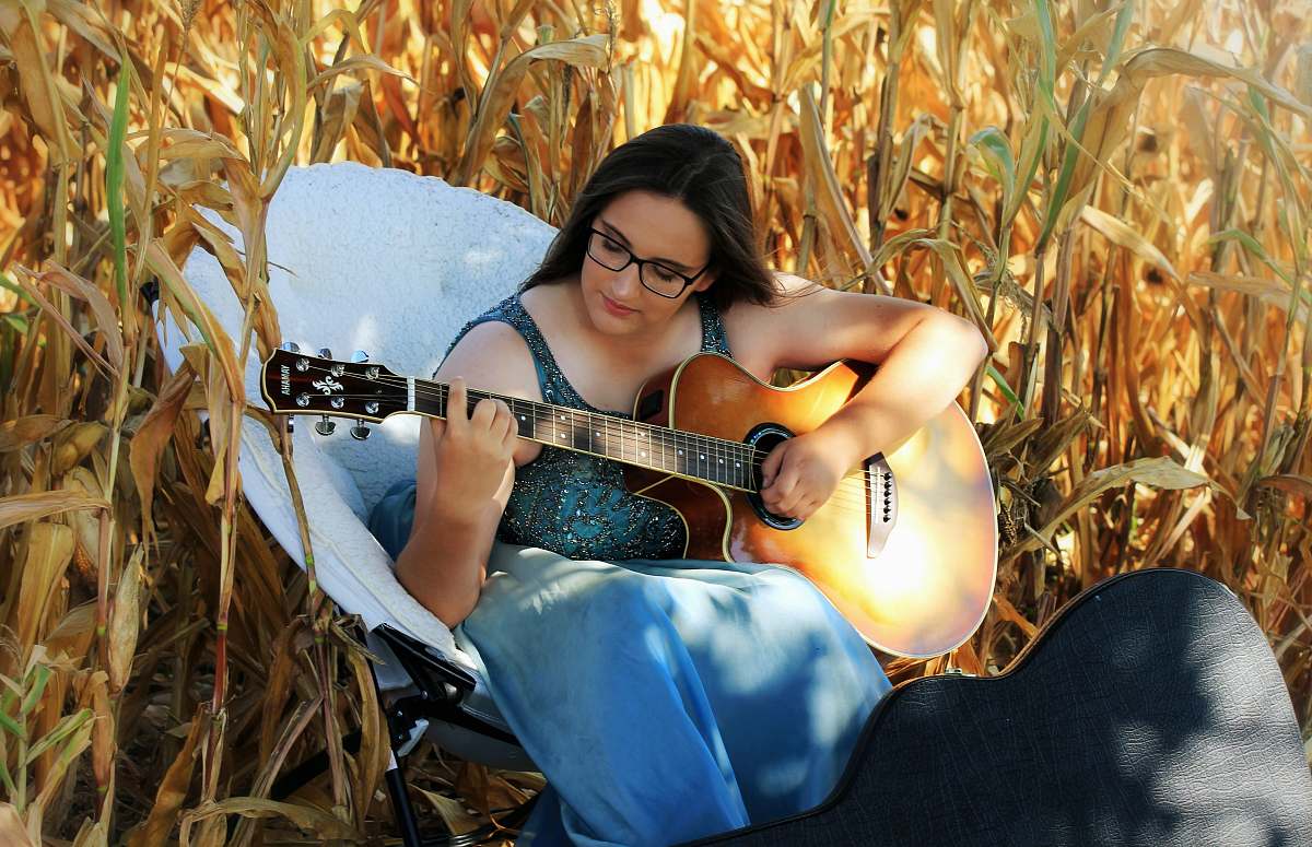 leisure activities woman playing guitar sitting on white chair on corn field musical instrument